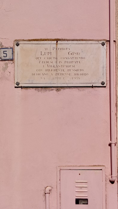 Lapide commemorativa dedicata a Lupi, affissa su una parete rosa.