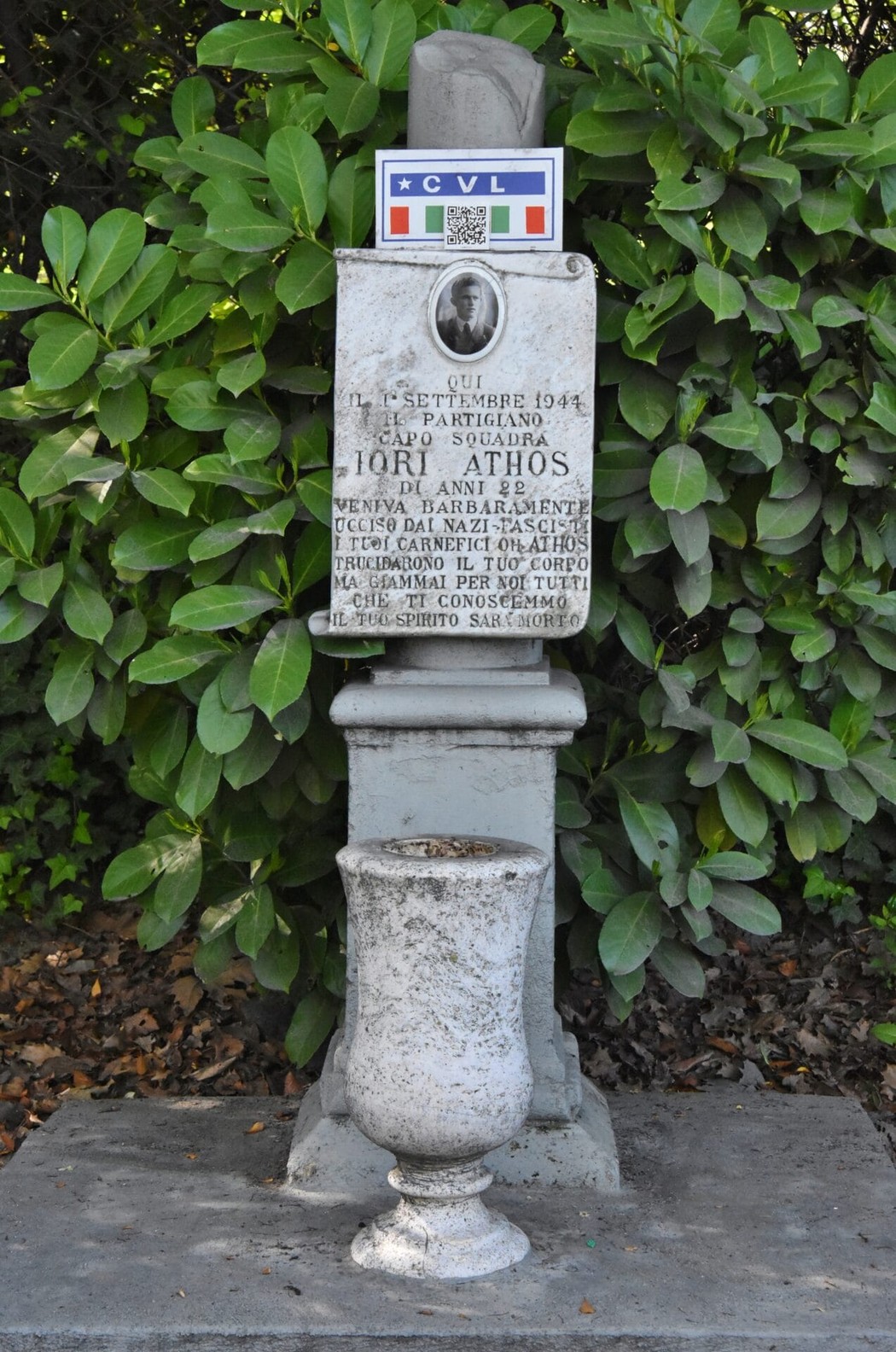 Cippo commemorativo dedicato a Jori Athos, situato tra la vegetazione, con dettagli storici e decorativi.