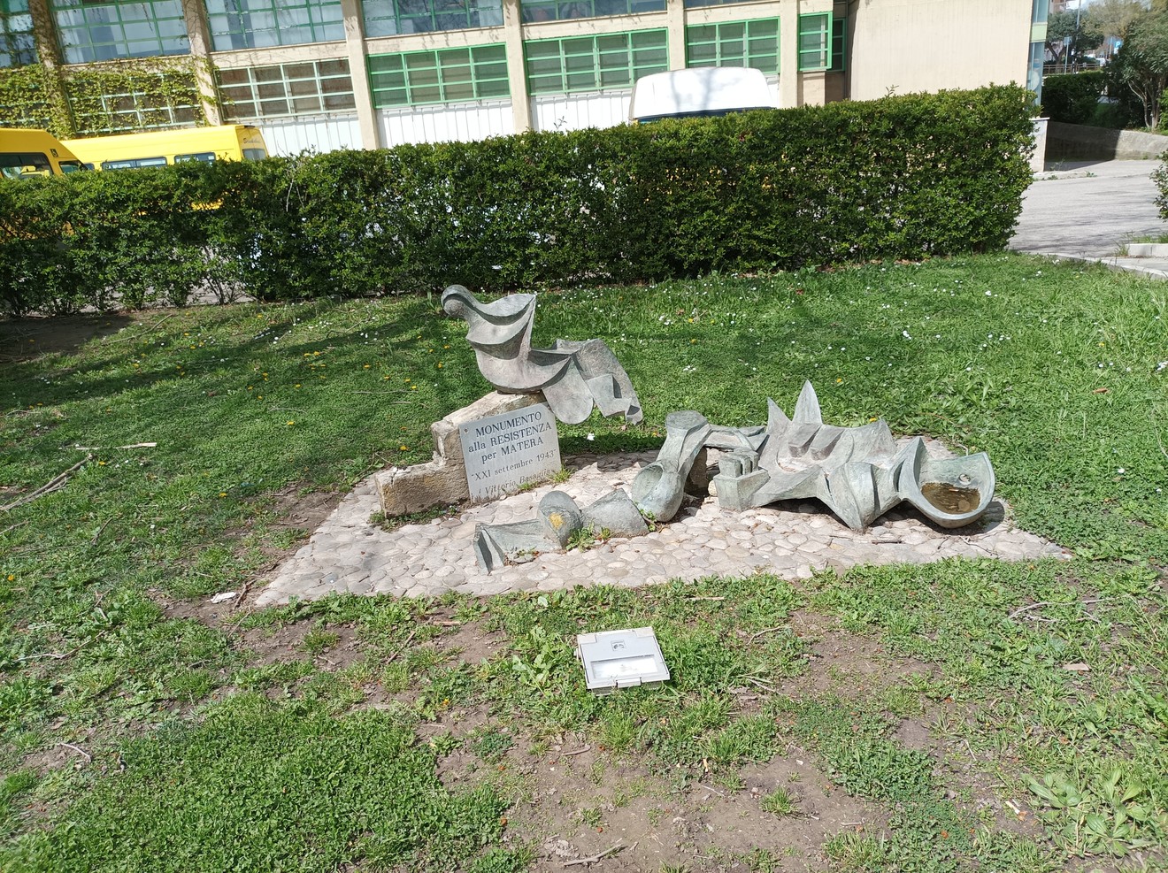 Monumento alla Resistenza, scultura in metallo con elementi astratti su base di pietra, circondata da verde.