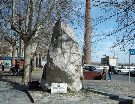 Monumento a Riberi: grande masso incastonato in un'area pubblica, circondato da alberi e persone.