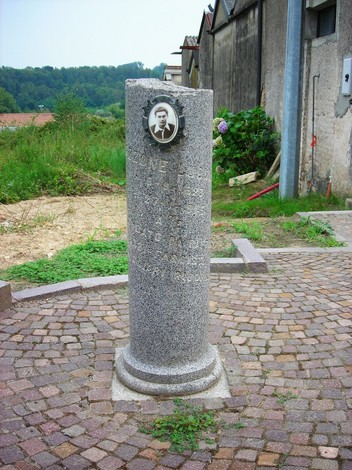 Cippo commemorativo in pietra con targa e scritte, situato in un'area verde e tranquilla.