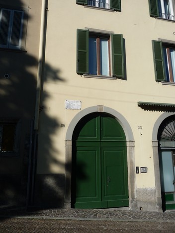Lapide dedicata ai caduti antifascisti in una facciata di edificio con porte verdi e finestre.