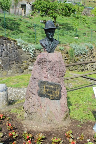 Cippo commemorativo con busto in bronzo su base di pietra in un contesto naturale.