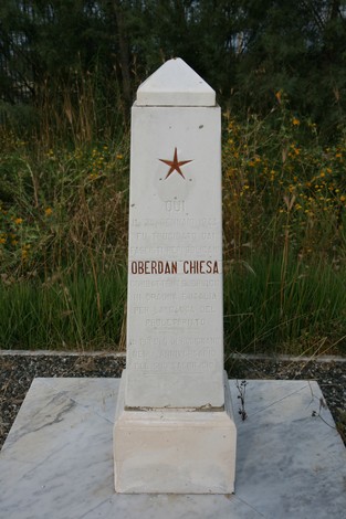 Cippo commemorativo dedicato a Oberdan Chiesa, immerso nella natura circostante.