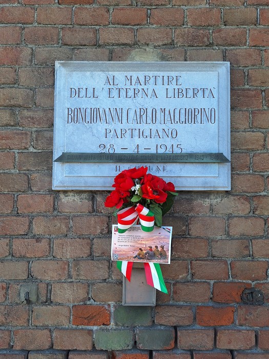Lapide commemorativa di Bongiovanni Carlo Maggiorino, decorata con fiori rossi e bandiera italiana.