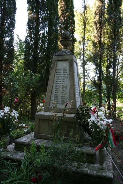 Monumento commemorativo dedicato alle vittime dell'eccidio di Guardistallo e Montescudaio, circondato da fiori.
