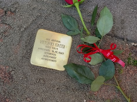Pietra d'inciampo dedicata a Vittorio Bassi, con una rosa e un nastro rosso accanto.