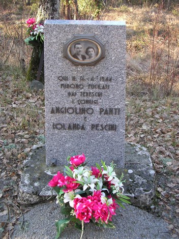 Cippo commemorativo dedicato a Angiolino Panti e Iolanda Pescini, con fiori sul monumento in un ambiente naturale.
