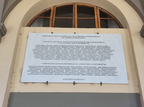 Lapide con iscrizione affissa sopra un portico, sotto una finestra ad arco con persiane in legno.