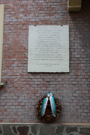 Lapide commemorativa di una base partigiana con una corona di alloro ai piedi, affissa su un muro di mattoni.