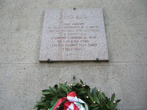 Lapide commemorativa dedicata a Rossi, con una corona di alloro e nastro tricolore, simbolo di onore e memoria.