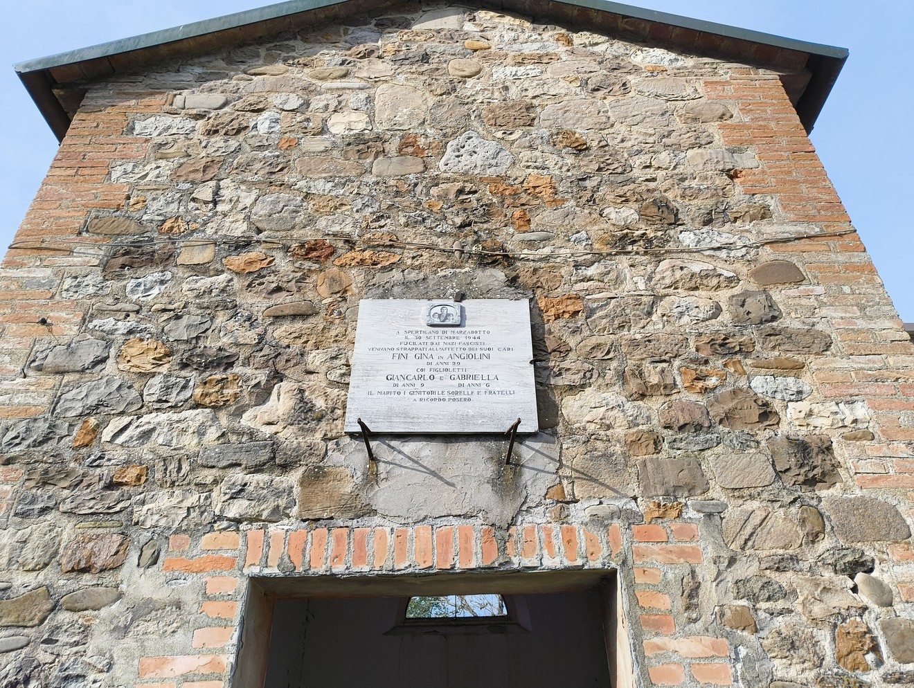 Lapide commemorativa agli Angiolini, incastonata in una muratura di pietra e mattoni.