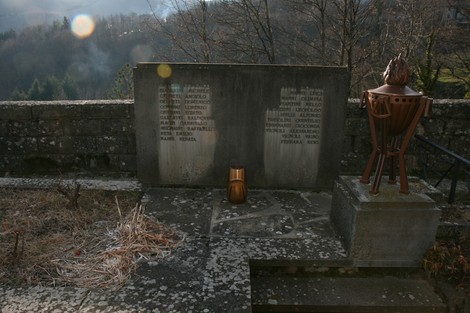 Monumento ai caduti, con lapidi commemorative e fiamma eterna in un contesto naturale.
