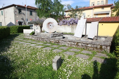 Monumento ai caduti di Soci, immerso nel verde, con pietre e lastre commemorative di fronte a un edificio.