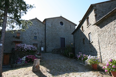 Stradina acciottolata tra edifici in pietra, adornata da fiori colorati e ombre di alberi.
