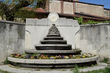 Monumento commemorativo dedicato ai caduti nei campi di prigionia, con una struttura a gradini e fiori colorati.