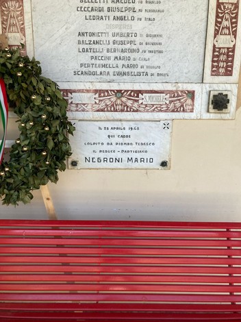 Lapide commemorativa dedicata a Mario Negroni, con una corona di fiori, situata in un monumento.