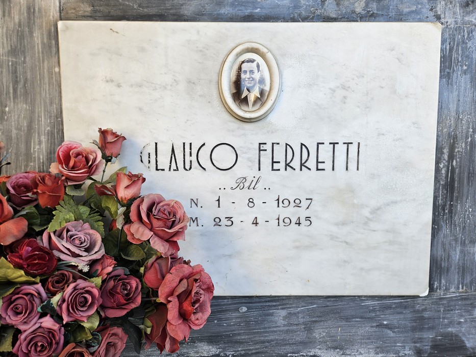 Lapide marmorea con ritratto ovale e iscrizione, decorata con un mazzo di rose ai piedi.