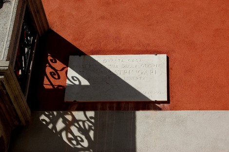 Lapide commemorativa a Stringari su parete arancione, con ombre e dettagli architettonici in evidenza.