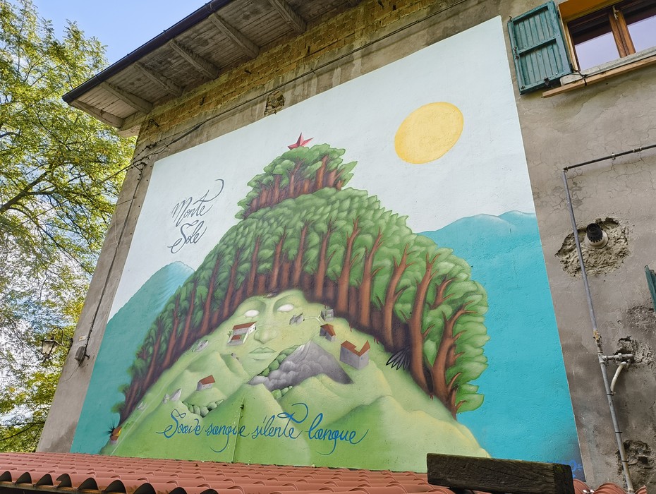 Murale colorato che rappresenta un paesaggio montano con alberi e una stella rossa, simbolo di comunità e natura.