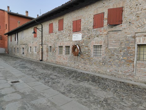 Lapide commemorativa su un edificio storico a Colle Ameno, con decorazioni floreali e finestre rosse.
