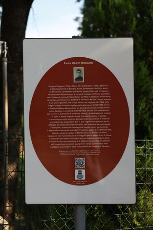 Cippo commemorativo dedicato a Padre Mario Ruggeri, con informazioni sulla sua vita e opera.