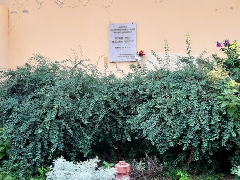 Lapide commemorativa dedicata a Valli e Robotti, circondata da vegetazione e fiori.