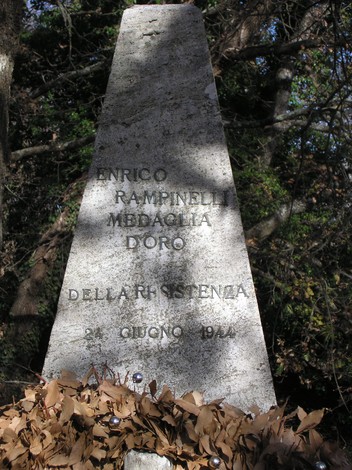 Cippo commemorativo dedicato a Enrico Rampinelli, Medaglia d'Oro della Resistenza, circondato da vegetazione.