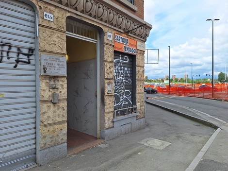 Ingresso di un edificio con scritte graffiti, accanto a un cantiere con recinzione arancione.