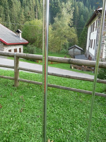Monumento ai Dodici Caduti circondato da vegetazione e edifici in un paesaggio montano tranquillo.