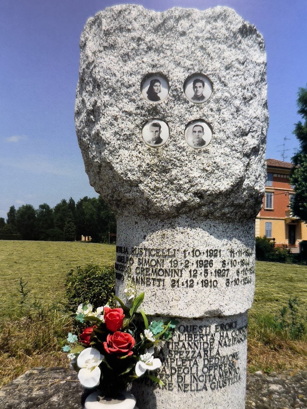 Cippo commemorativo con foto di Rusticelli, Simoni, Cremonini e Nannetti, circondato da fiori e campagna.