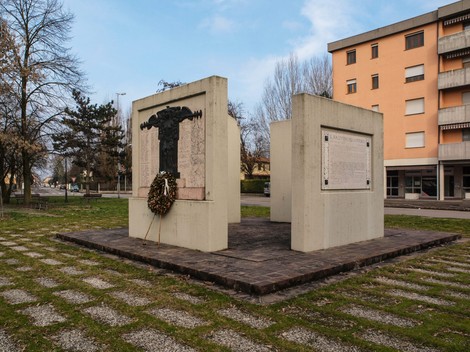 Monumento ai caduti di Novi, dedicato alla memoria dei combattenti, circondato da un prato e edifici.