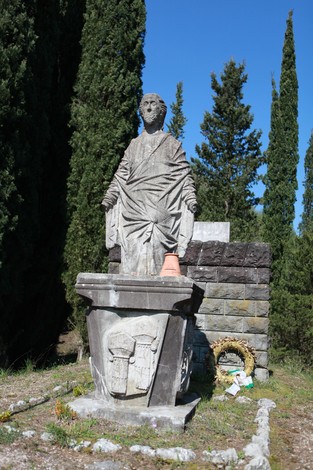 Monumento ai caduti di Purocielo, statua in pietra con dettagli e alti cipressi sullo sfondo.