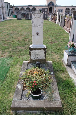 Sepolcro di Vavassori, con monumento bianco e aiuola di fiori, situato in un cimitero con diverse tombe circostanti.