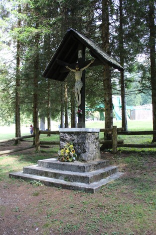 Crocifisso dei Partigiani, monumento situato in un'area verde circondata da alberi, con fiori ai piedi.