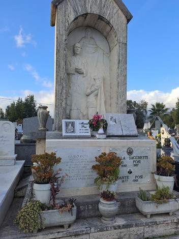 Sepolcro di Posi, con statue commemorative e decorazioni floreali, immerso in un cimitero.