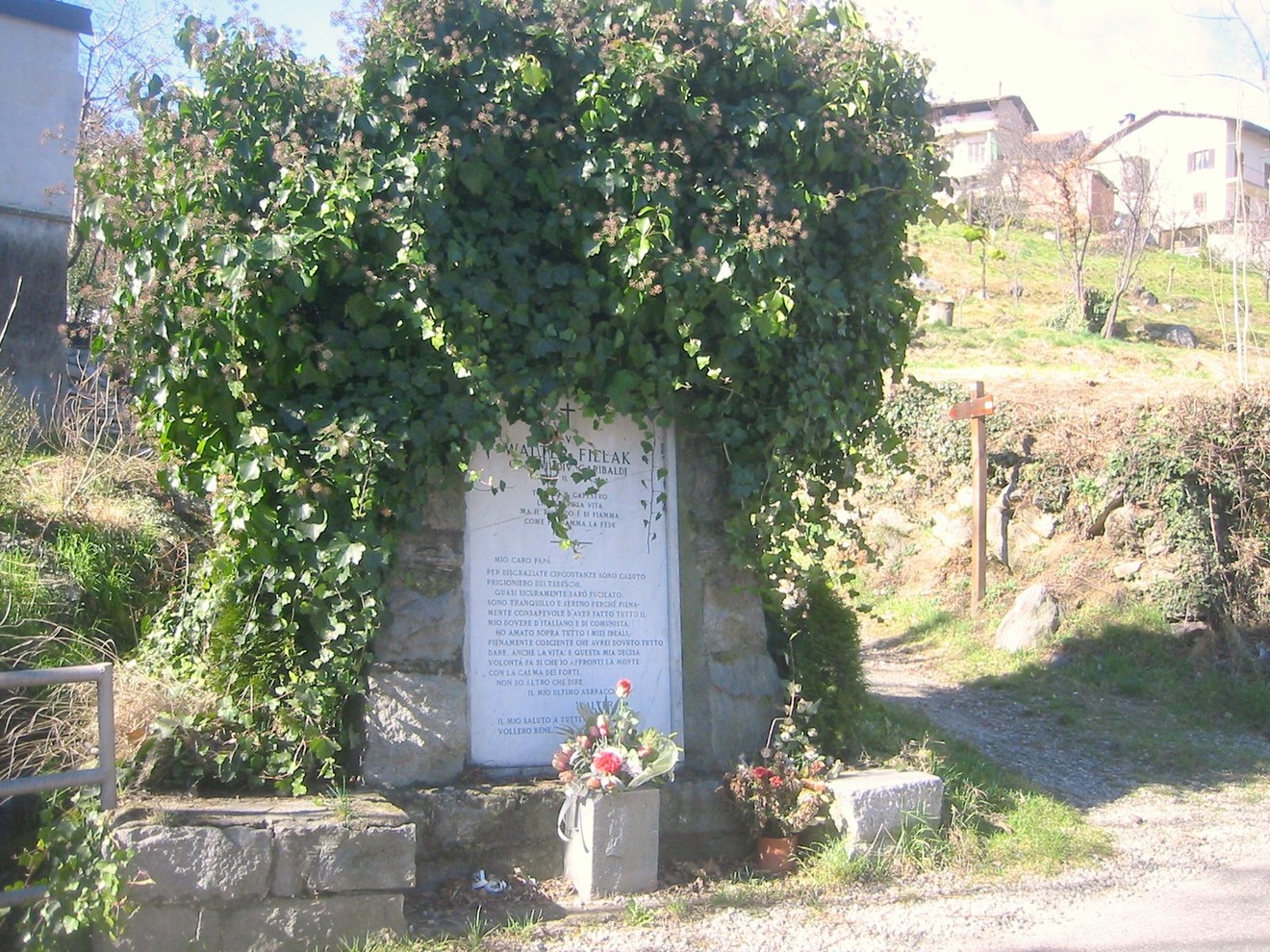 Monumento a Fillak, immerso nel verde, con decorazioni floreali e cordoglio per la memoria.
