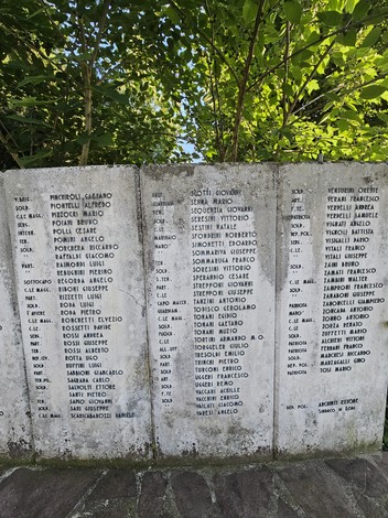 Monumento ai Caduti con nomi incisi su una parete di pietra circondata da verde.