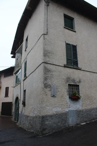 Immobile rurale con facciata in intonaco, finestre con persiane verdi e dettagli architettonici storici.