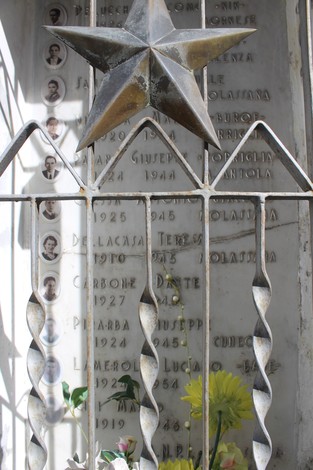 Cappella ai caduti di Molassana con decorazioni metalliche e iscrizioni commemorative. Fiori adornano l'area.