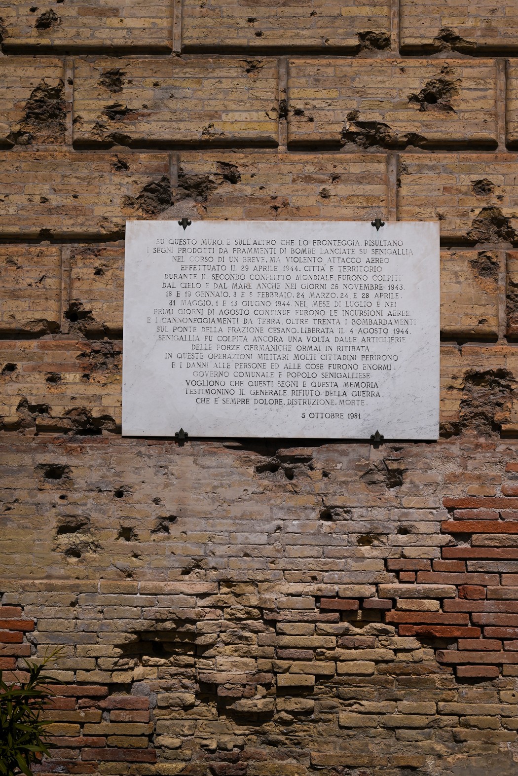 Lapide in memoria dei caduti durante i bombardamenti, affissa su un muro vissuto e segnato dal tempo.