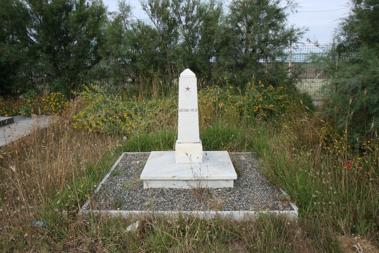 Un cippo storico in un'area naturale, circondato da erba e fiori selvatici.