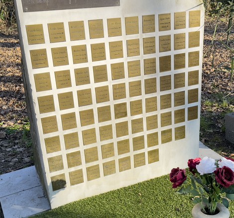 Il Giardino della Memoria con lastre commemorative su una parete, circondato da vegetazione e fiori.