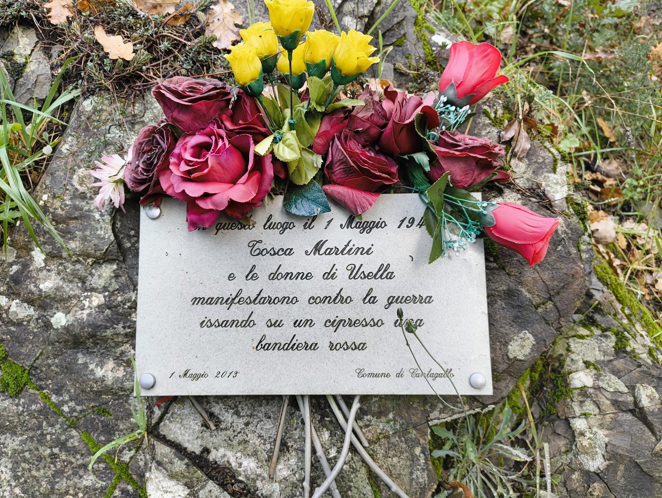 Targa commemorativa dedicata a Cosca Martini e alle donne di Usella contro la guerra, adornata con fiori.