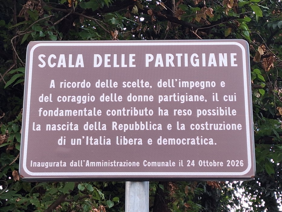 Targa marrone con iscrizione su palo metallico, dedicata alla Scala delle Partigiane, tra alberi.