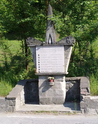 Monumento commemorativo dedicato a Bagni, Ganapini e altri, circondato da verde e situato lungo una strada.