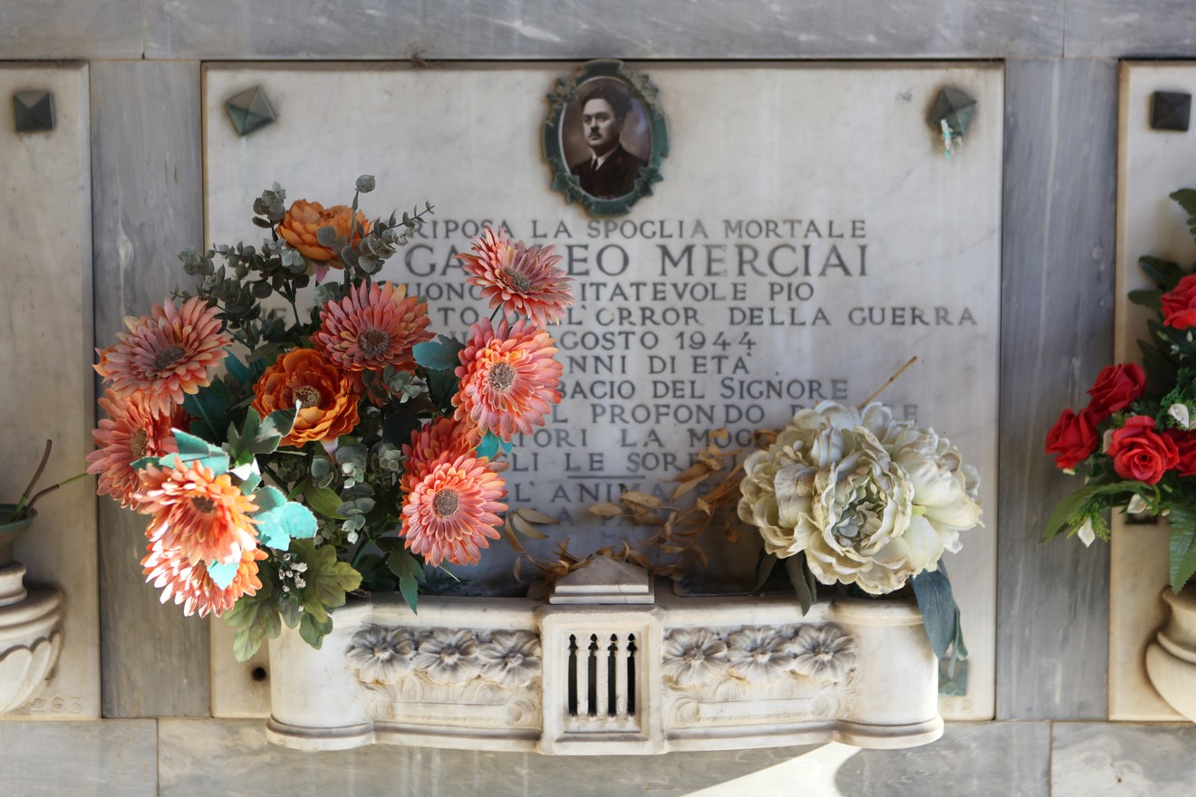 Sepolcro di Merciai con decorazioni floreali e lapide commemorativa. Atmosfera di rispetto e memoria.