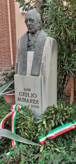 Statua di don Giulio Minardi, commemorativa, circondata da vegetazione e nastri tricolori.