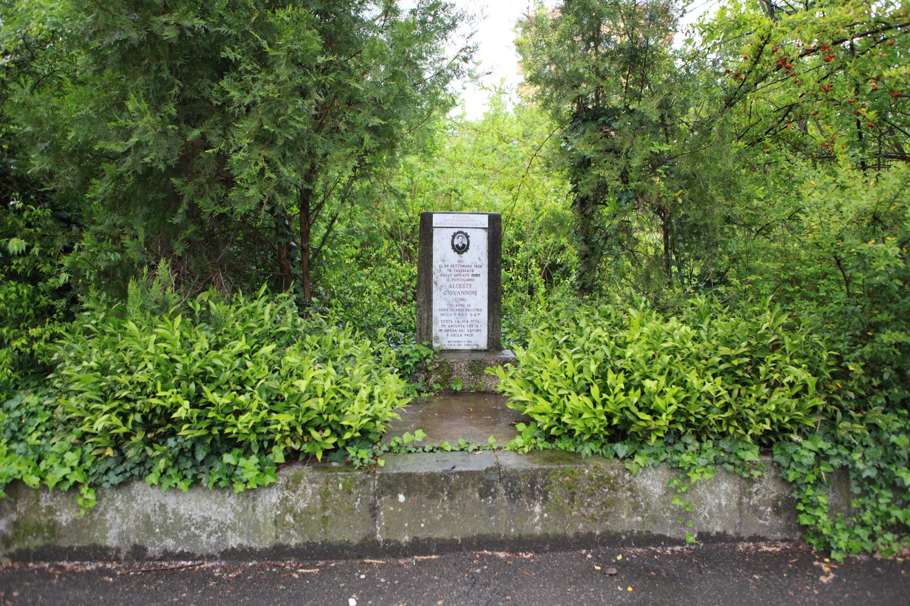 Cippo commemorativo immerso nel verde, circondato da piante e alberi. Un elemento di memoria storica.