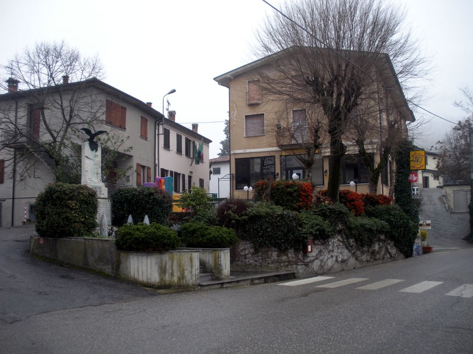 Monumento ai caduti di Canevino, situato all'incrocio del paese, circondato da piante e edifici.